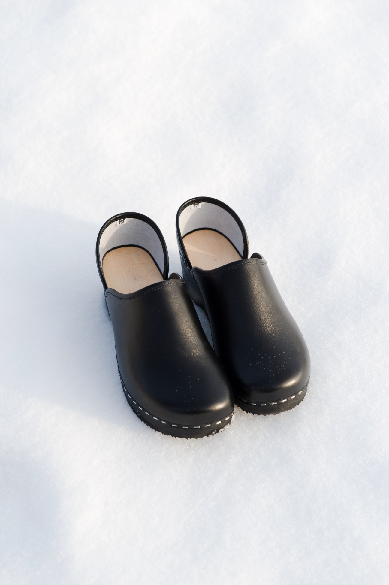 Pair of black leather Talla Puukenkä clogs with wooden soles on snow.