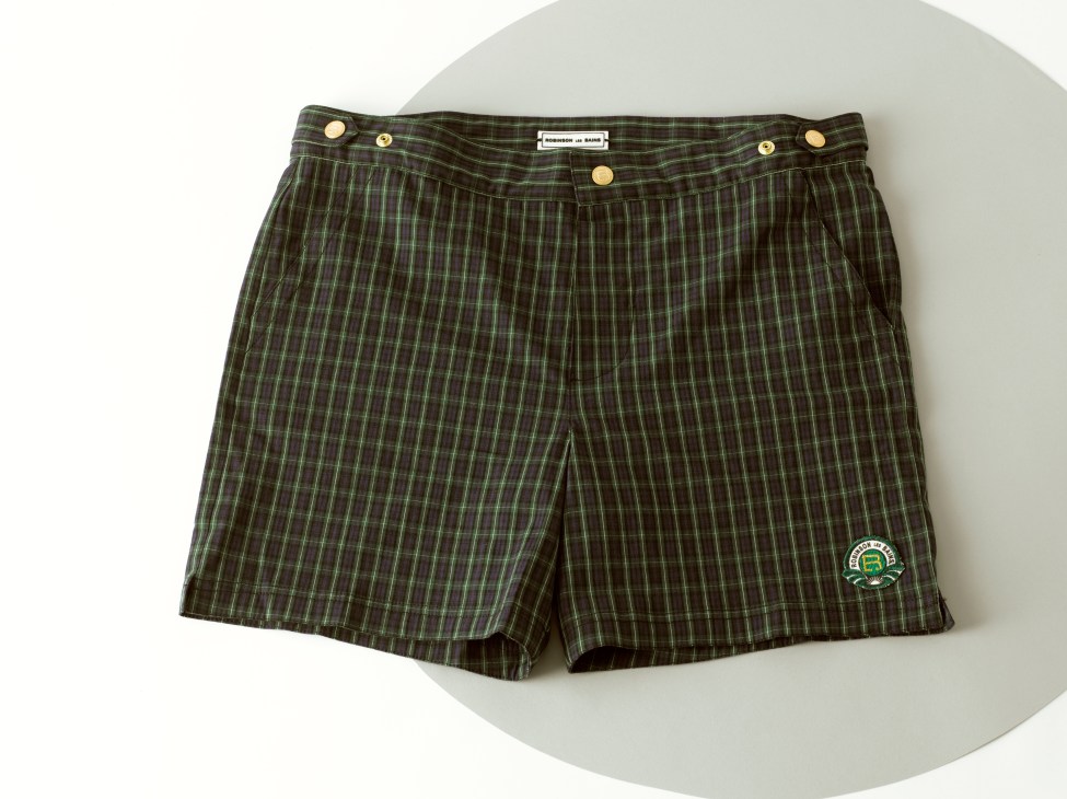 Tartan plaid shorts with brass buttons and green logo patch on white background.