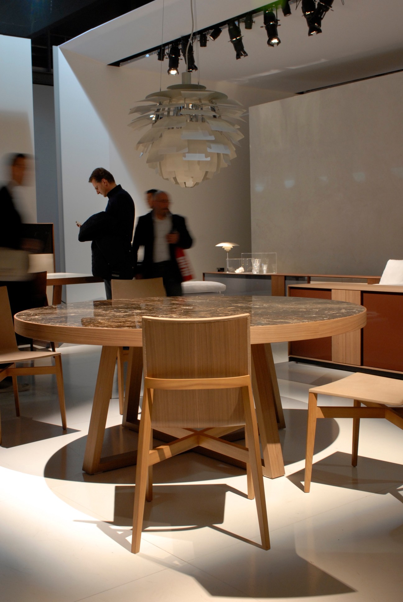 Marble-top table with wooden chairs by Rodolfo Dordoni for Molteni & C's 'W' series in a bright gallery space with hanging pendant light and blurred figures.