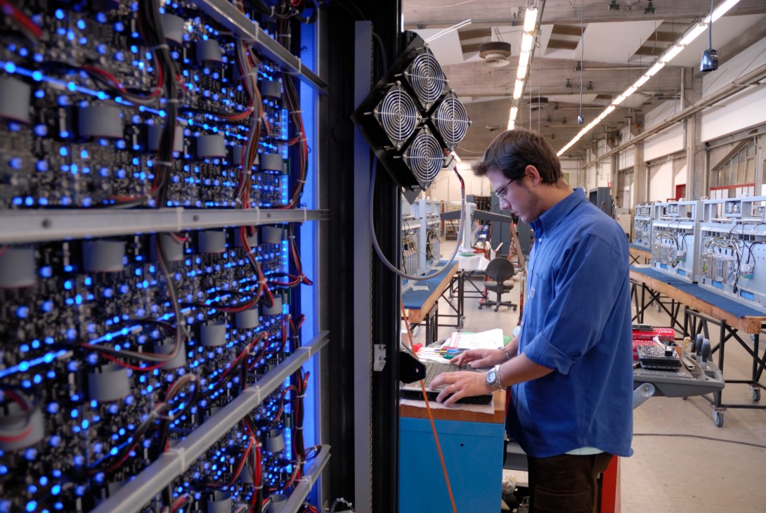 Technician in blue shirt testing LED motorway sign with illuminated blue lights in Solari factory.