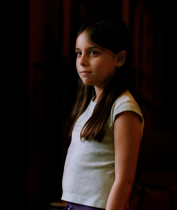 Portrait of Sofia Sabal, a 7-year-old student at Oslo International School, against a dark red background.