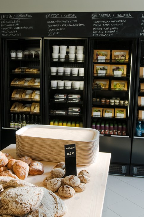 Artisanal breads and pastries displayed on a wooden table with a woven wooden basket and price tag at a Sis deli.