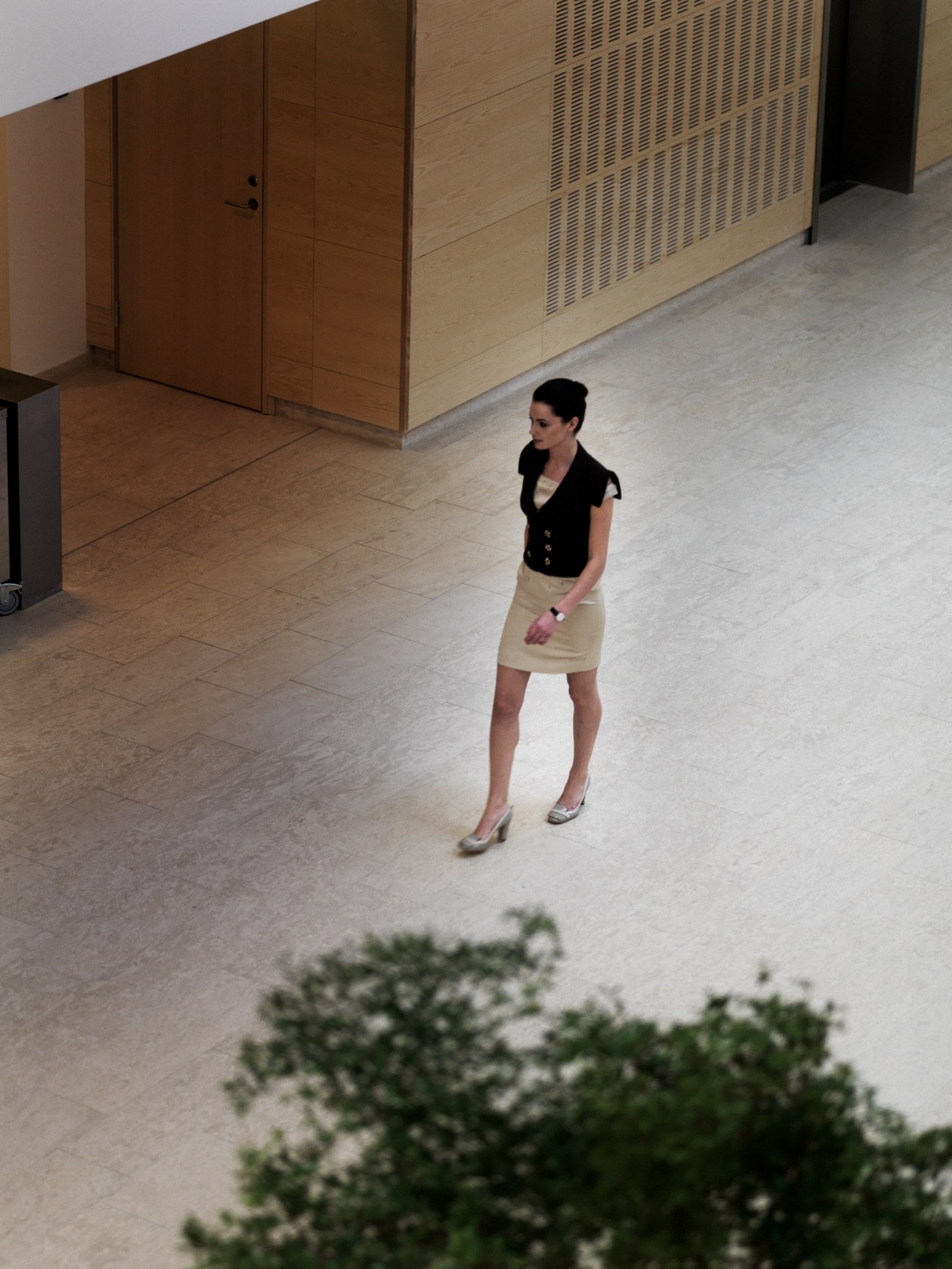 Woman in black waistcoat and silk dress standing in modern office foyer with wooden doors.