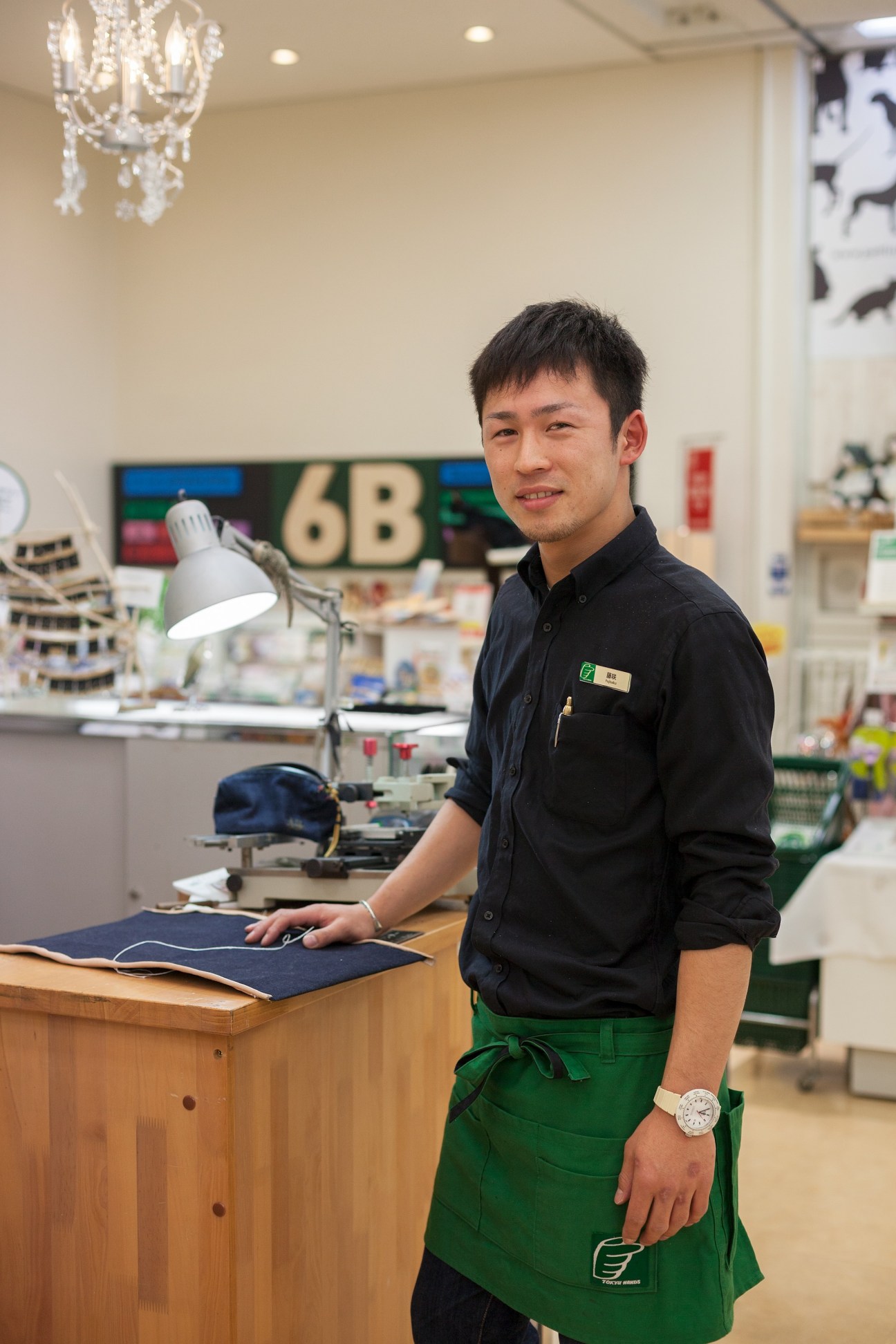 Jewellery repair man Kazuya Fujisaku wearing a green apron at his workstation in Tokyu Hands.