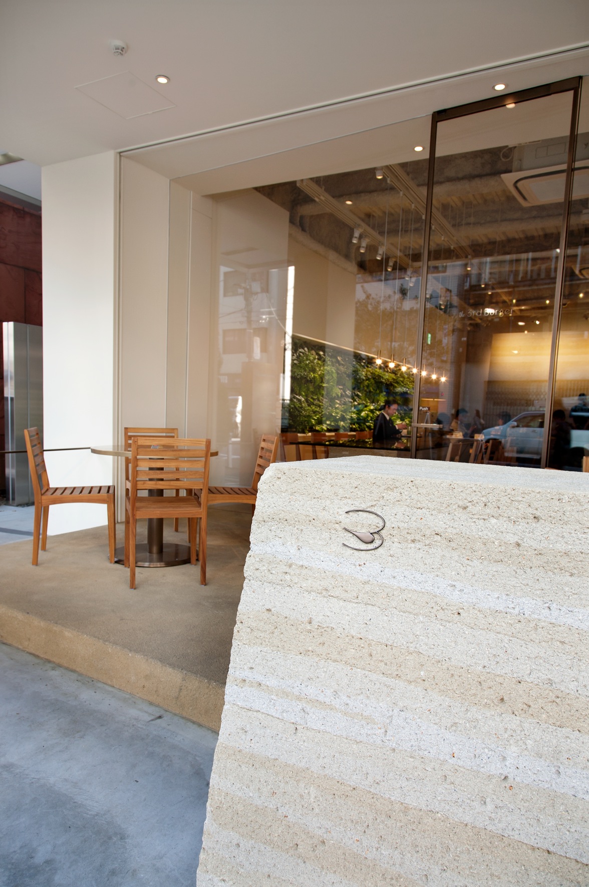 Modern restaurant interior with concrete counter, wooden chairs, and floor-to-ceiling windows at The 3rd Burger.