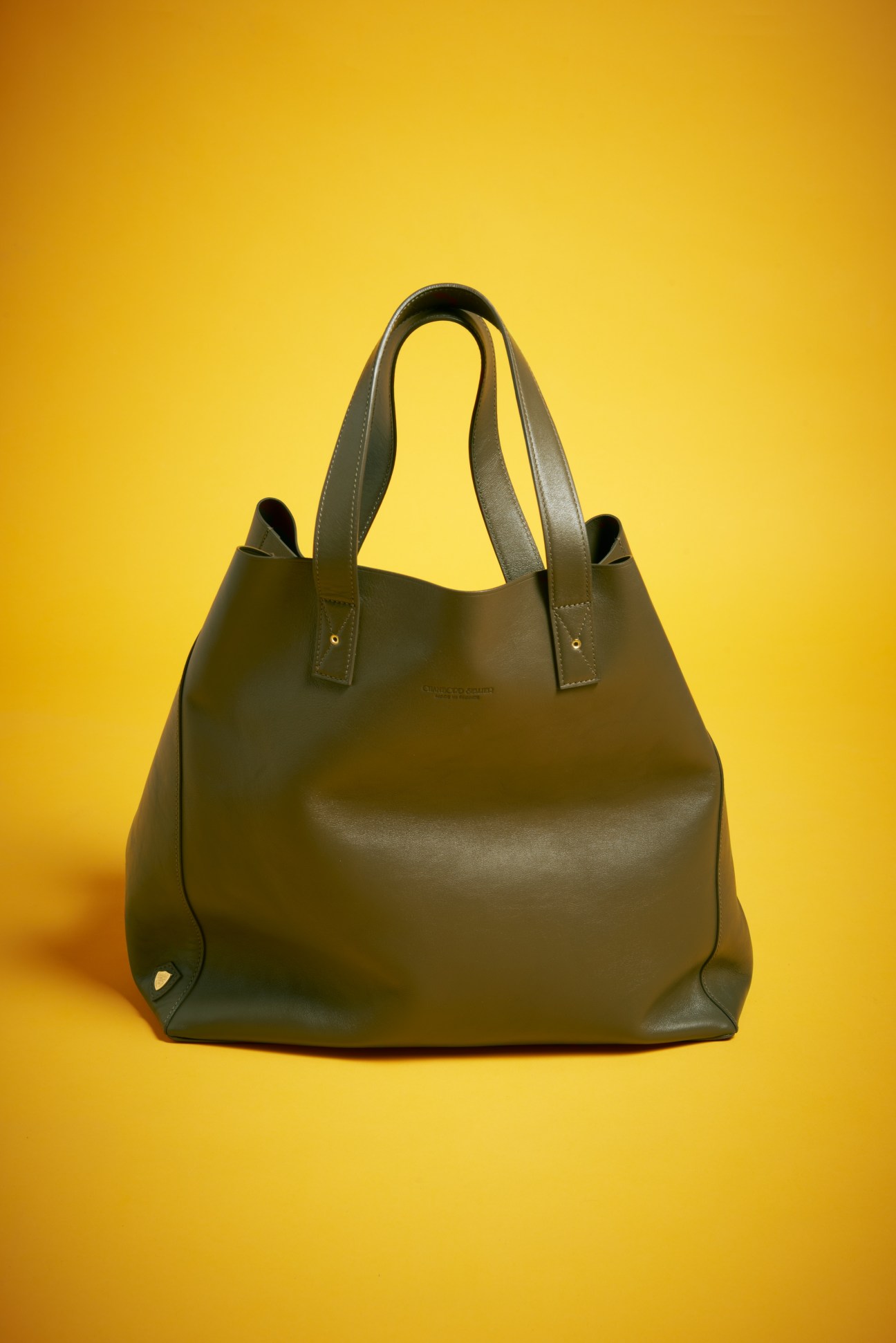 Olive green leather tote bag with dual handles against a yellow background.