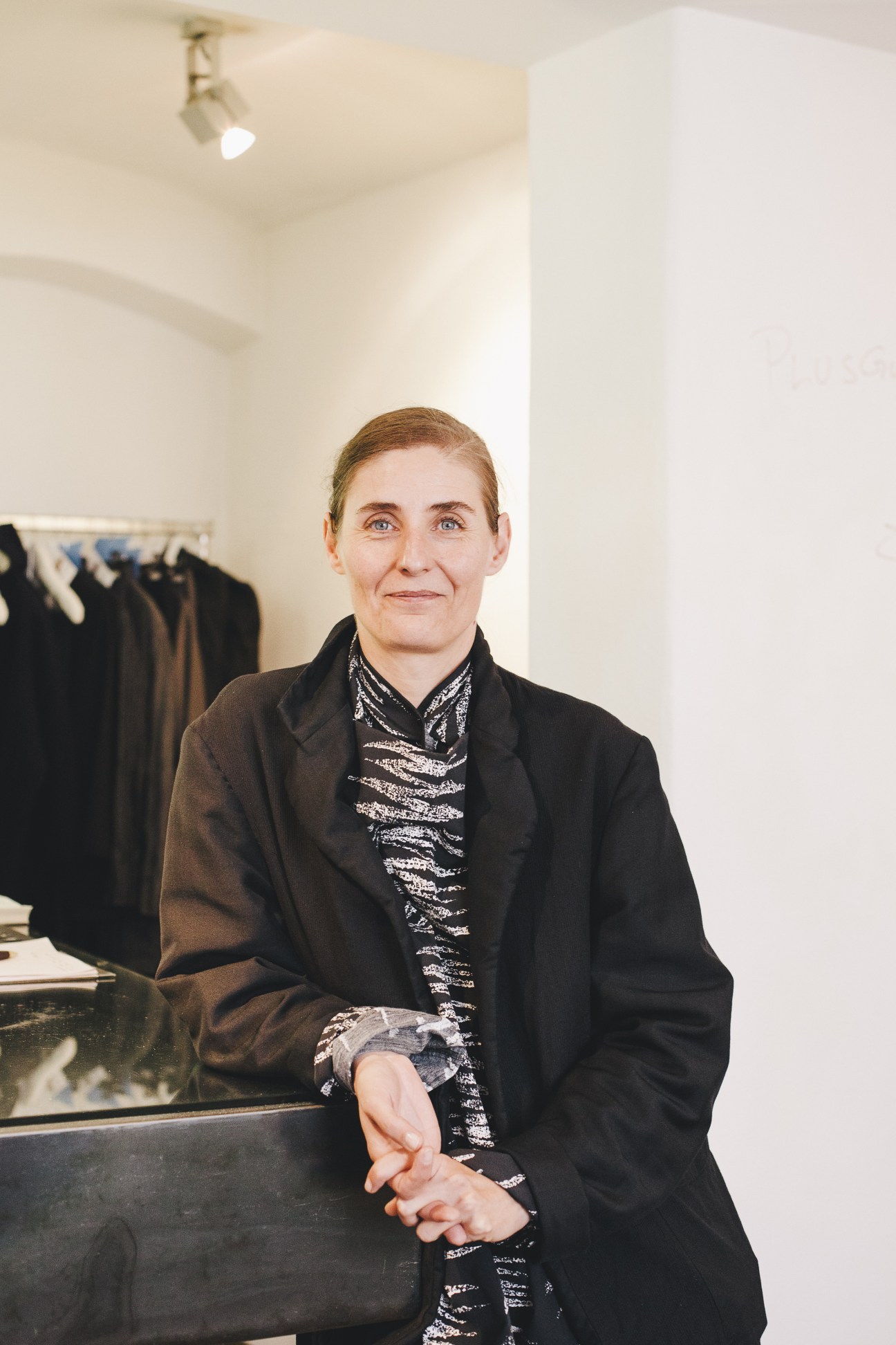 Woman in black blazer and patterned shirt standing in minimalist white retail space