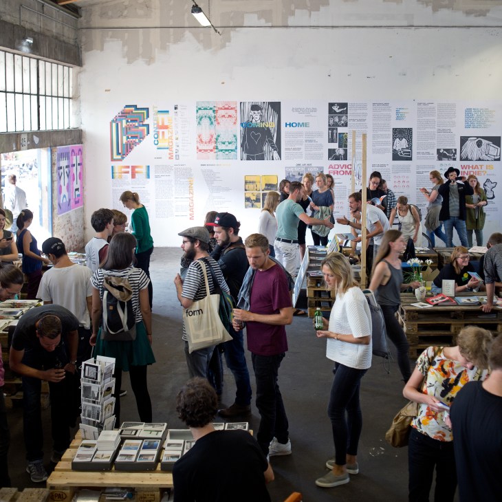 Large group of visitors browsing magazine displays and talking at Indiemagday event in industrial space