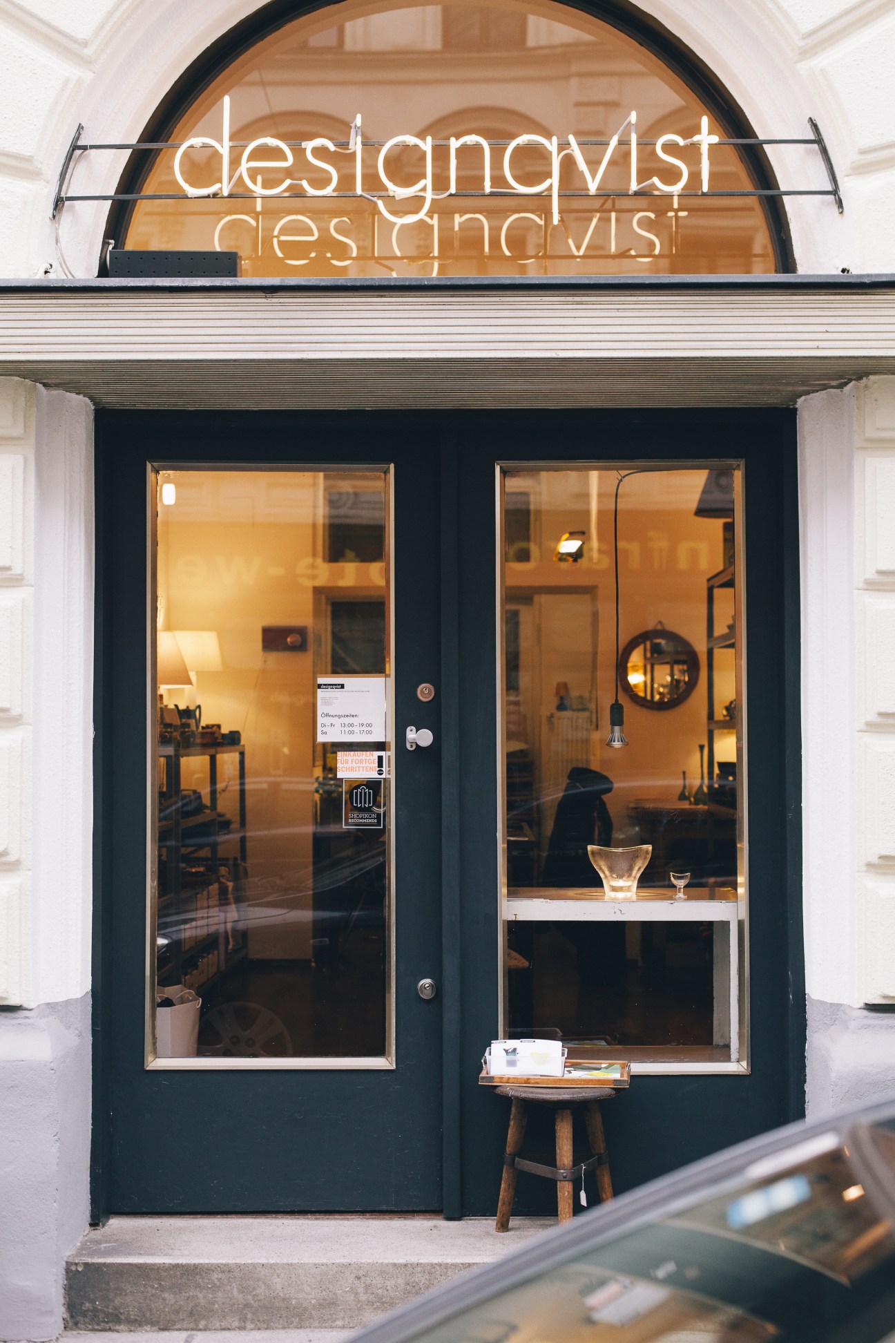 Designqvist storefront in Vienna with minimalist black frame and neon sign reflecting warm interior lighting.