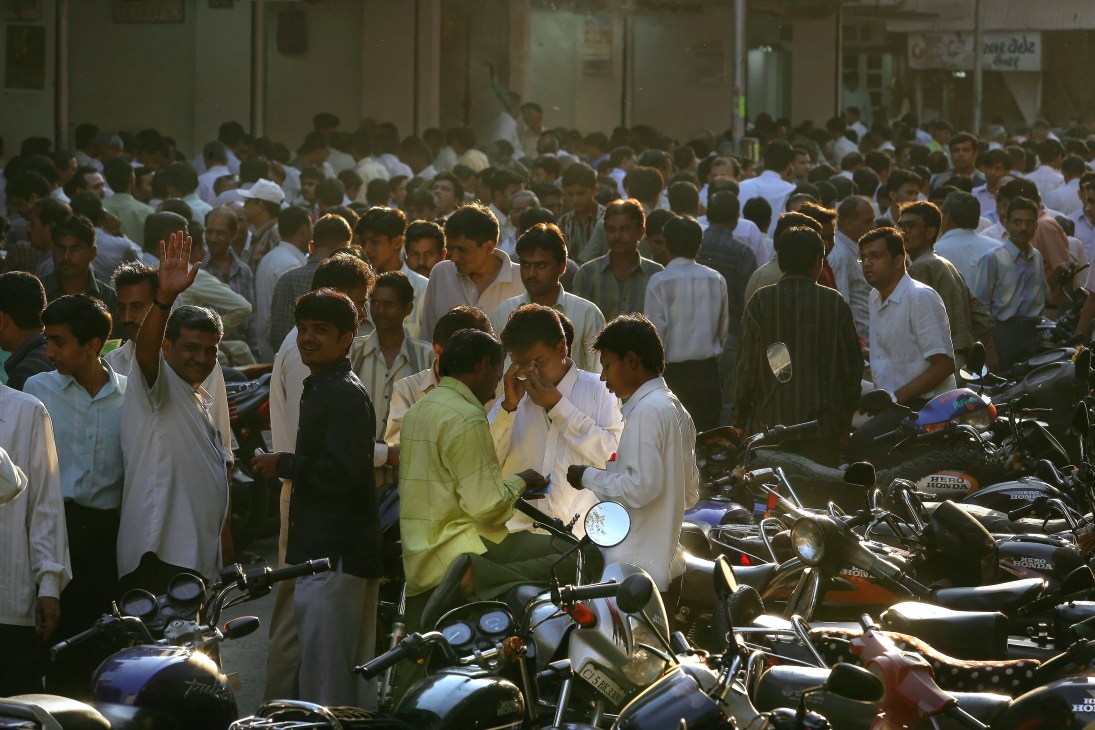 Crowded street scene in Surat, India with young people and motorcycles gathered together.