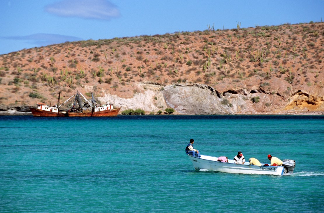 Fishing boats anchored in turquoise waters off an arid, rocky coastline in Mexico's Baja Peninsula.