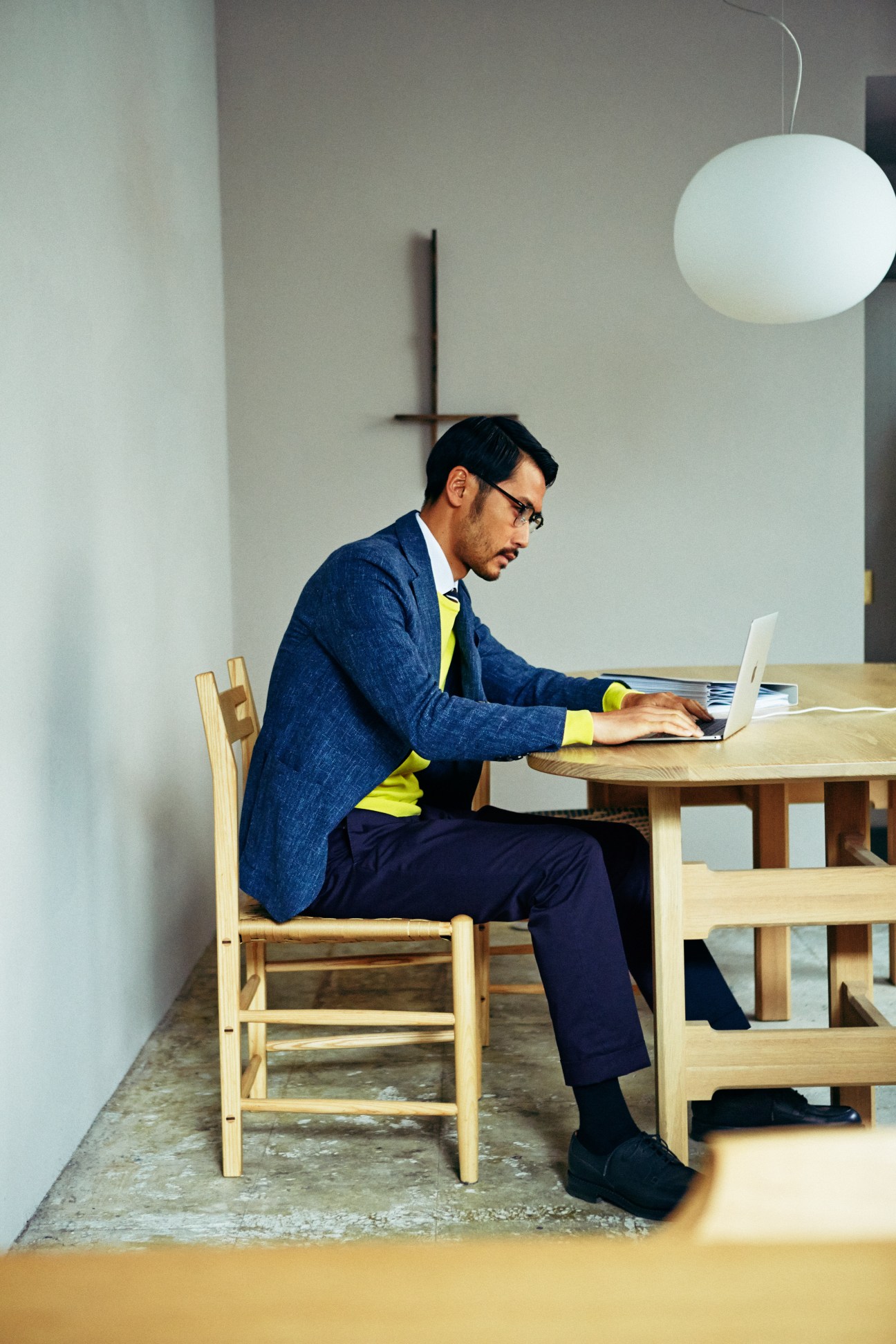 Man in blue Lardini jacket and yellow jumper working at laptop at wooden desk.