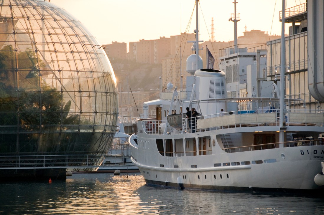 Classic 1960s motor yacht with white hull docked in urban waterfront setting with modern architecture.
