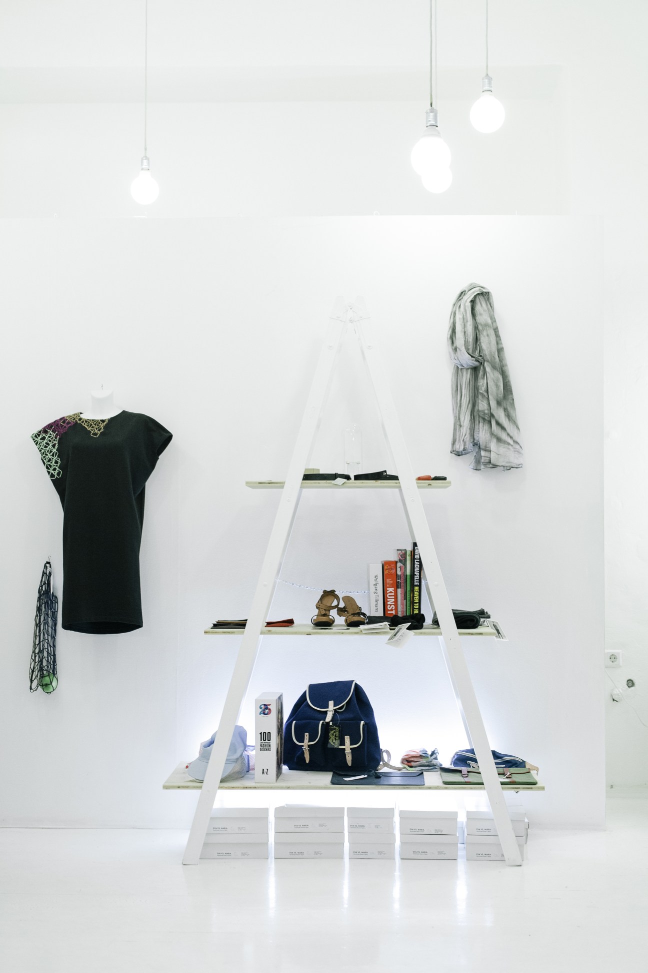 Minimalist fashion display with A-frame white shelving, clothing items, books, and accessories in S/ght store.