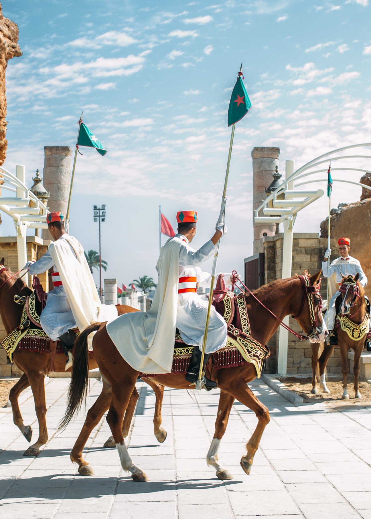Mounted guards in white robes and red hats carrying green and red flags at the mausoleum of Mohammad V in Rabat.