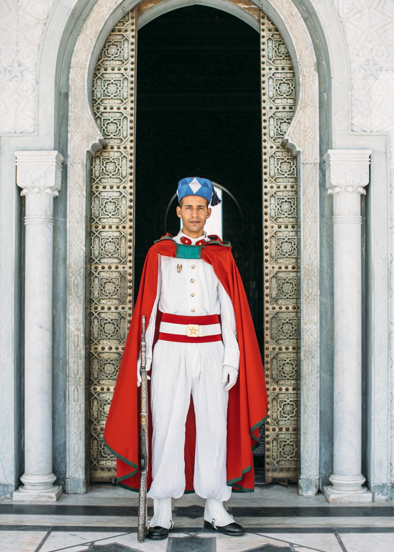 Guard in red and white ceremonial uniform standing at ornate palace archway in Rabat.