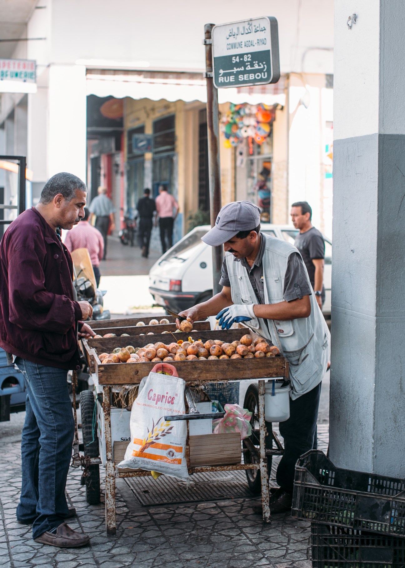 Street vendor selling onions from a wooden cart on a Casablanca street under a sign for Rue Sebou.