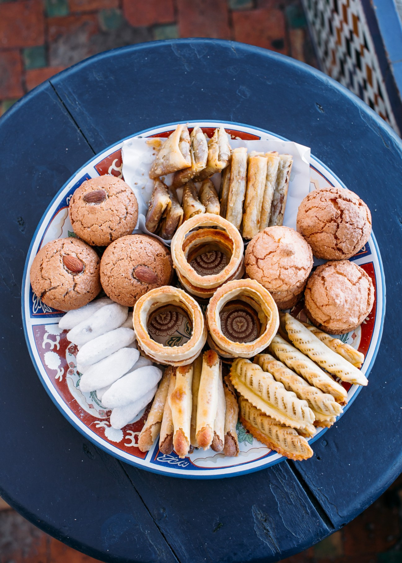 Overhead view of traditional Moroccan pastries and savory items arranged on a decorative plate with blue and red border.