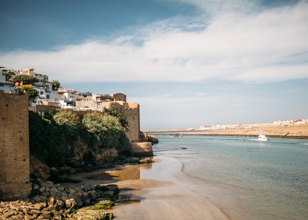 Coastal fortress town with stone buildings and white houses perched on cliffs above a sandy beach and turquoise waters.