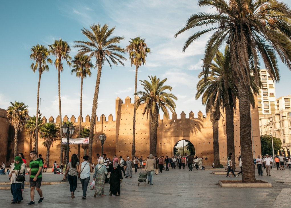 Entrance to Kasbah Oudayas Medina with visitors and palm trees under blue sky.