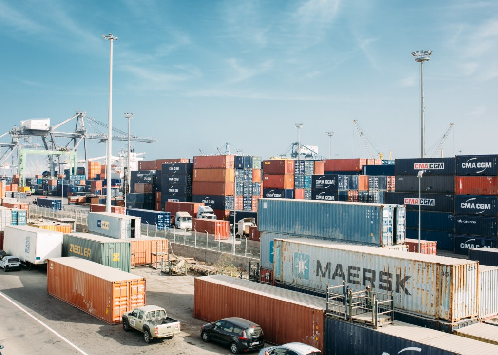 Stacked shipping containers labeled CMA CGM and Maersk at Casablanca's port with cranes and vehicles.