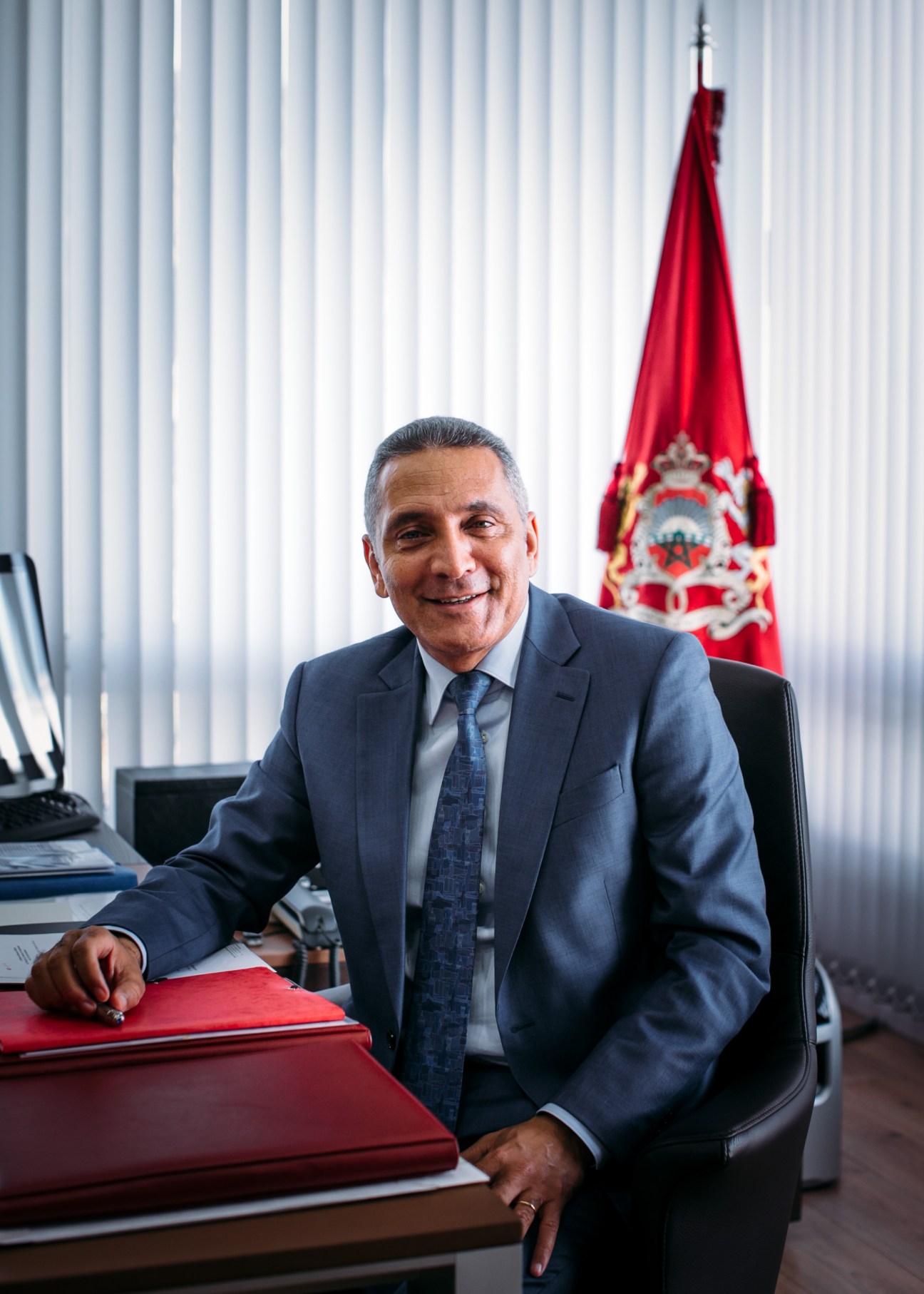 Moulay Hafid Elalamy, Moroccan minister for industry, trade, investment and the digital economy, smiling at his desk with a Moroccan flag behind him.