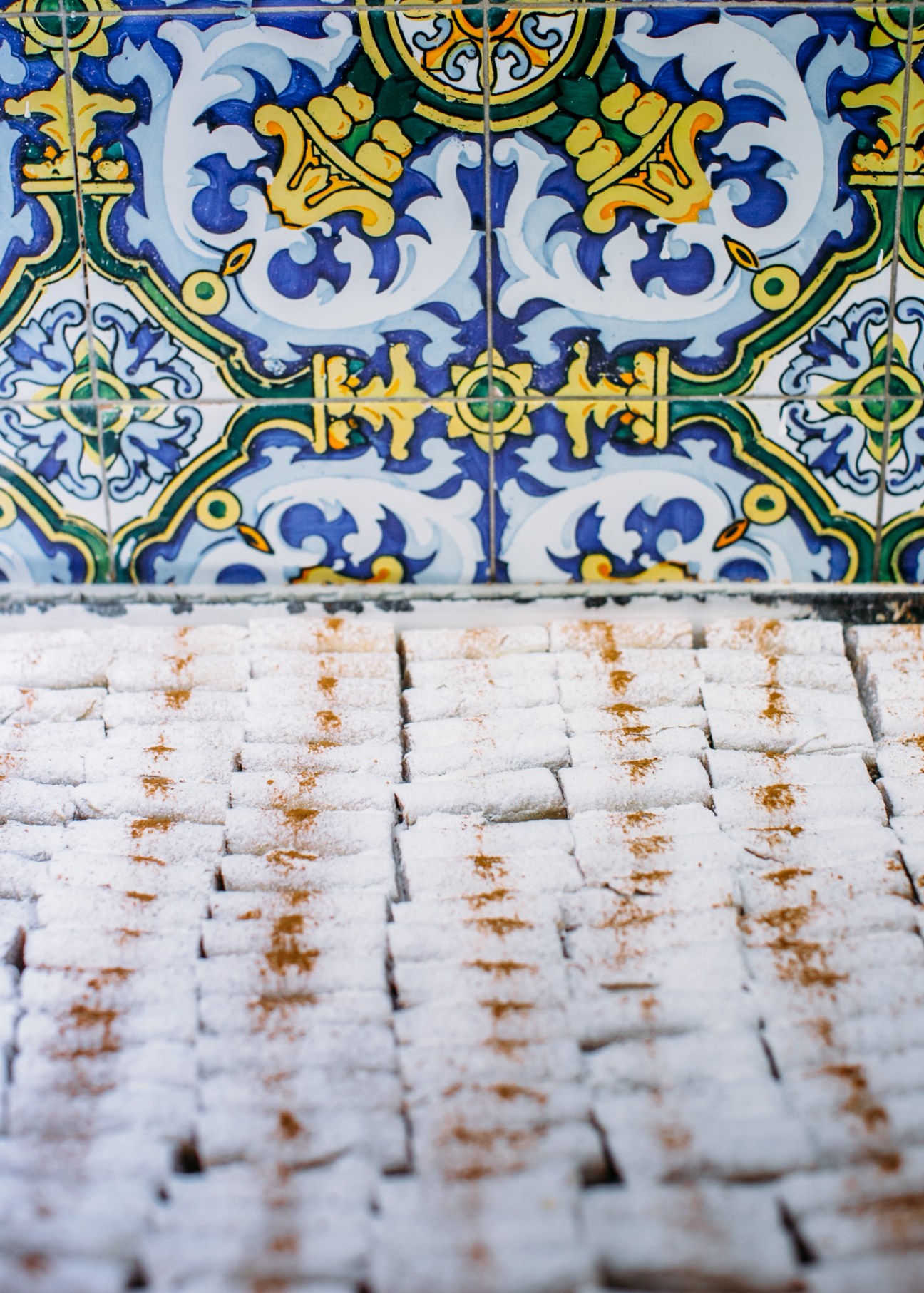 Decorative Moroccan tiles with intricate blue, yellow and green patterns above white pastries dusted with powdered sugar.