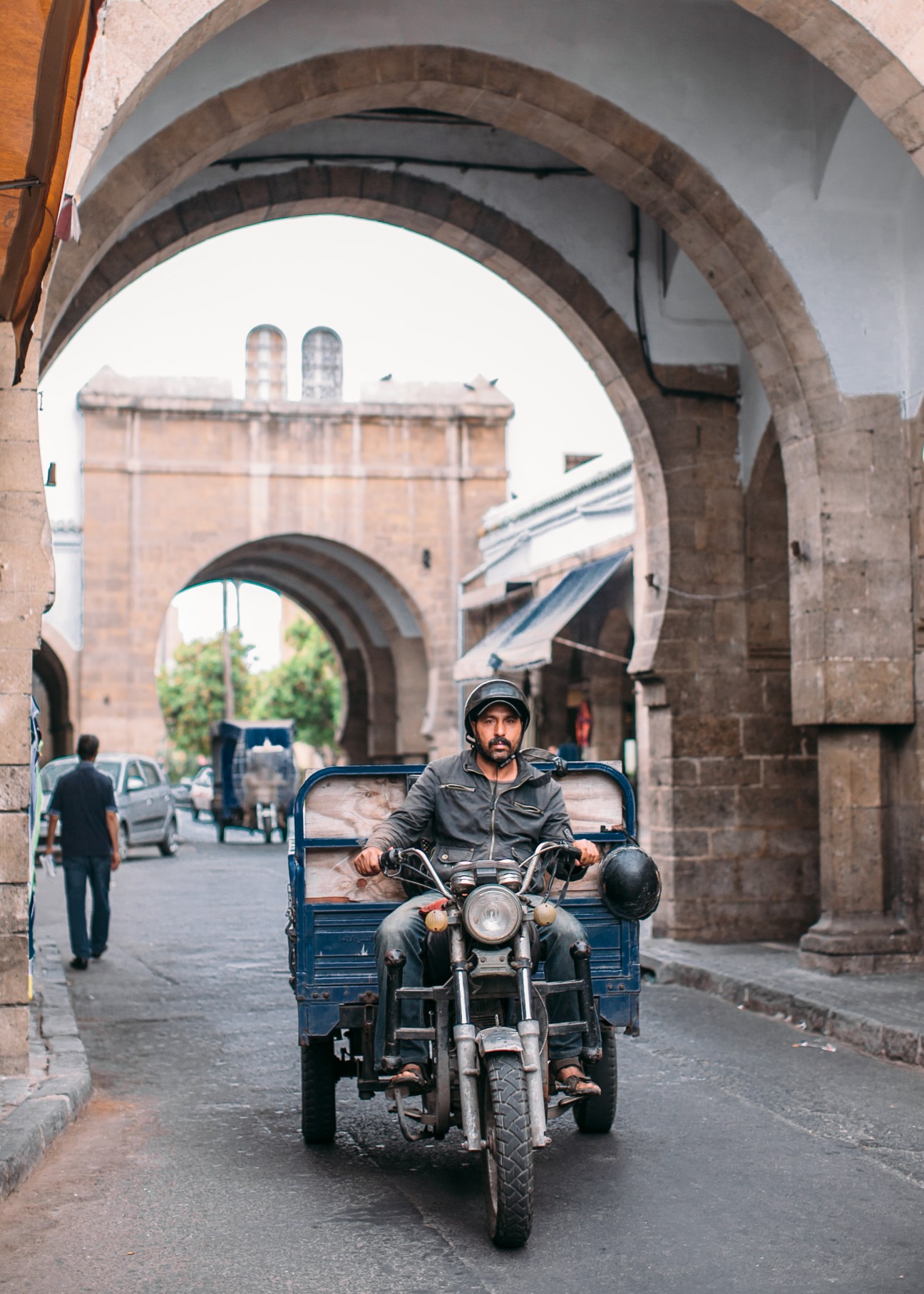 Man riding a motorcycle with sidecar through Casablanca's medina beneath stone archways.