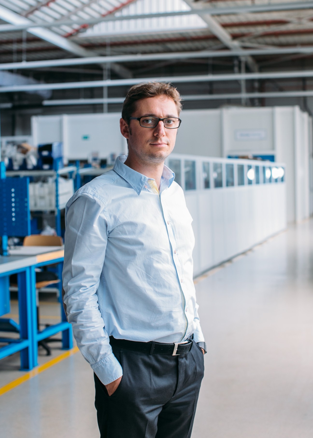 Man wearing glasses and light blue shirt standing in an industrial aerospace manufacturing facility.