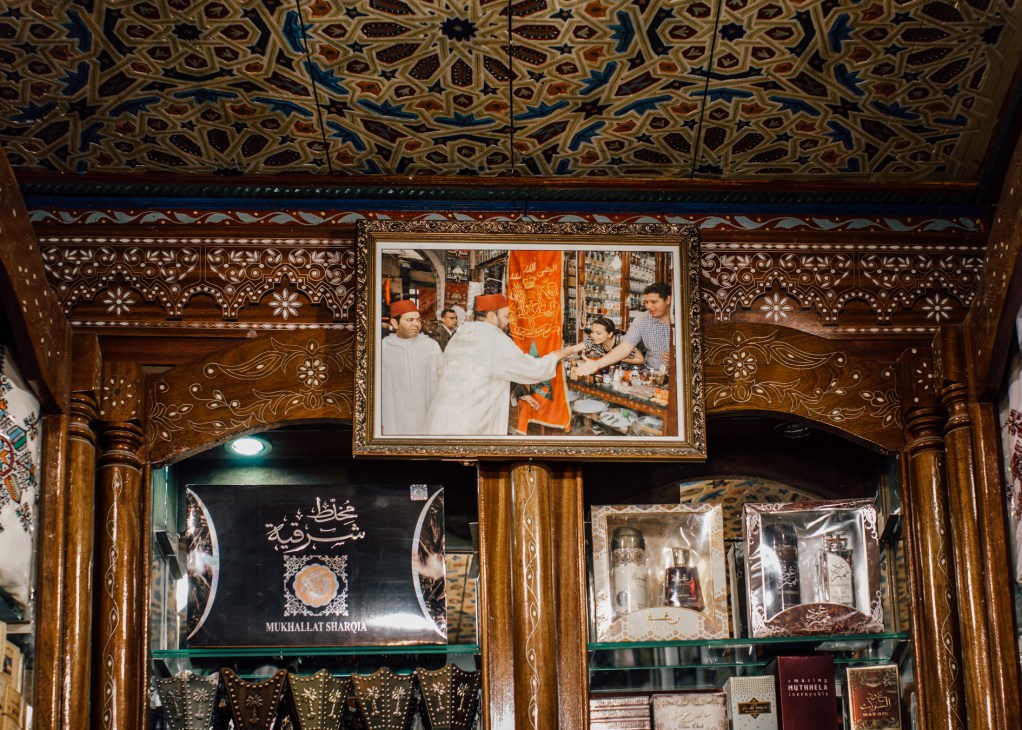 Mohammed VI portrait in ornate frame hanging above a perfumery shop display in Fes medina.