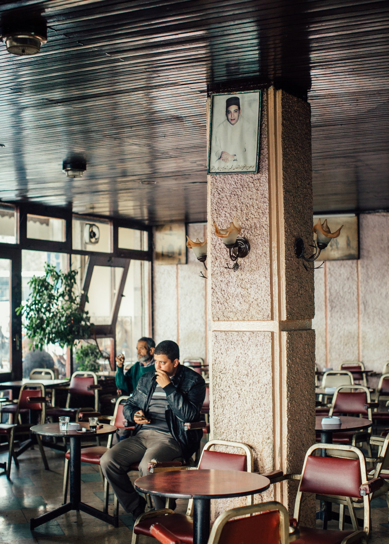 King Mohammed VI portrait hanging above a man seated in a Moroccan café