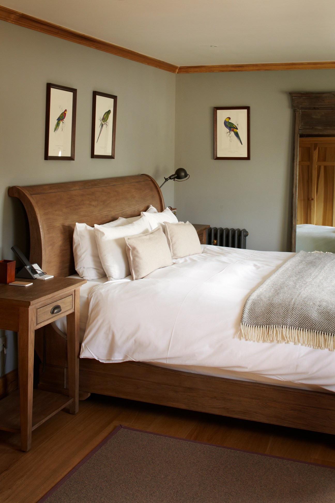 A neatly made wooden bed with white linens and cream pillows in a room with bird artwork on walls.