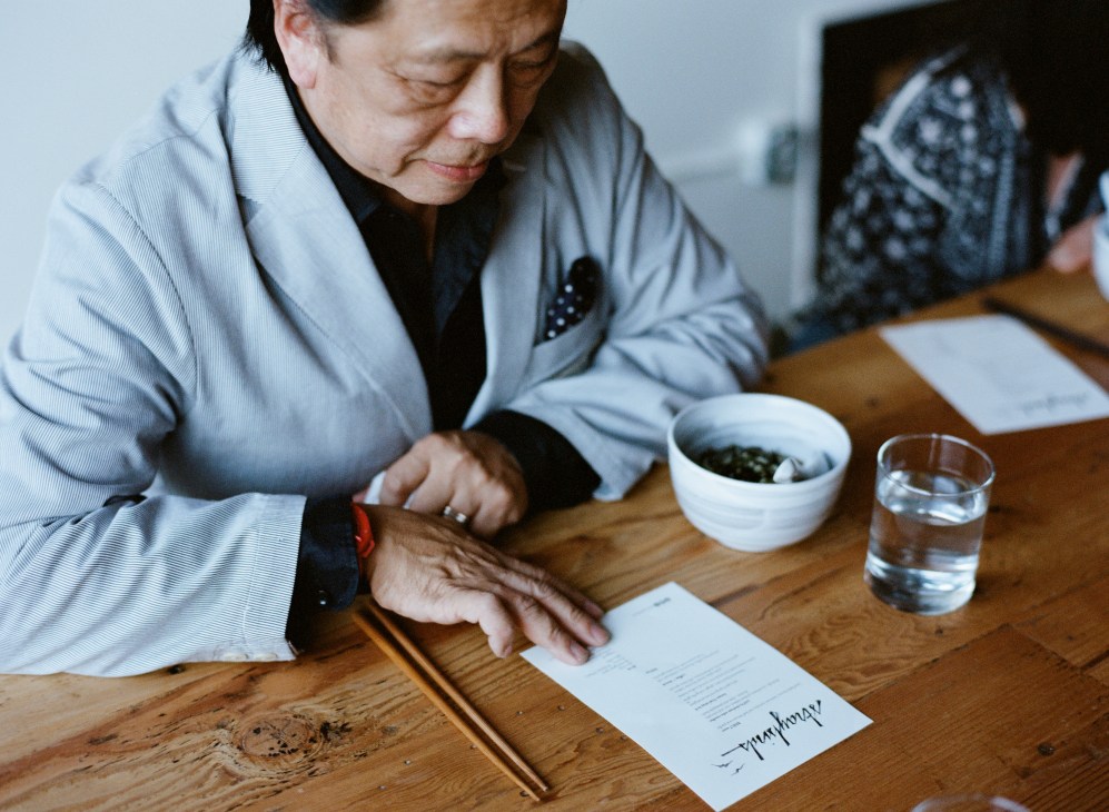 Man in light blue shirt reviewing a document at a wooden table with a bowl of food and water glass.