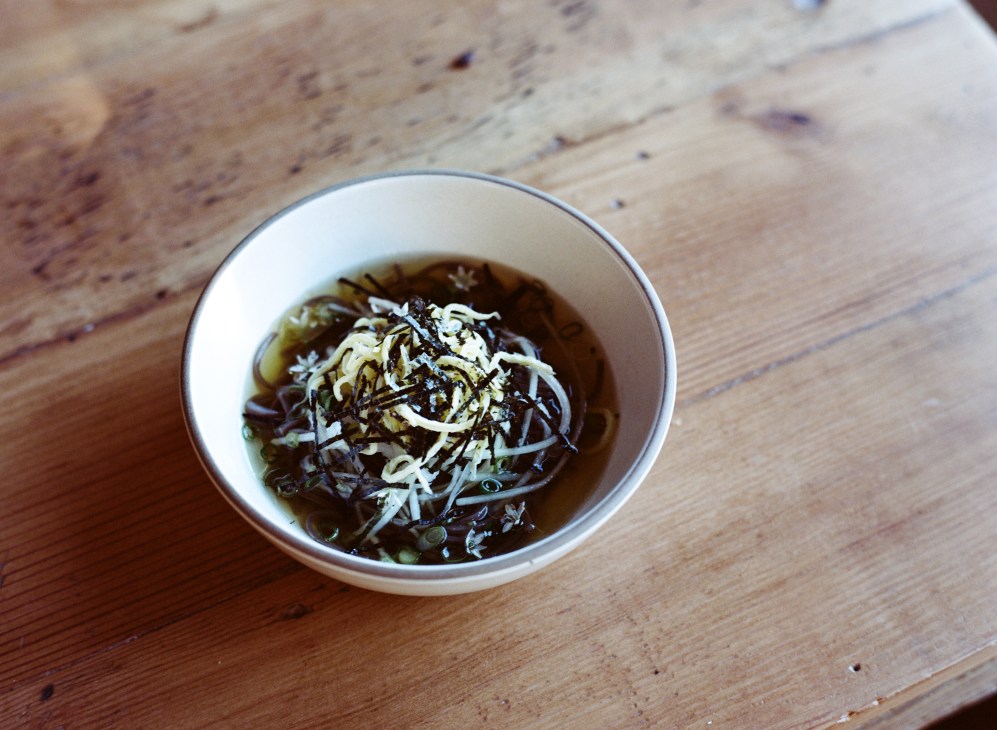 Cold buckwheat noodles with shredded garnish in a white bowl on a wooden table.