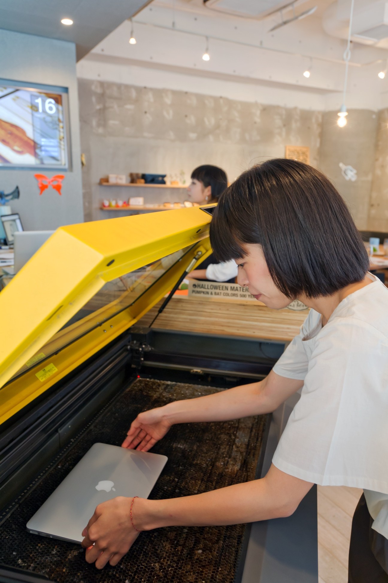 Woman operating a yellow laser cutter at FabCafe in Tokyo's Shibuya district.