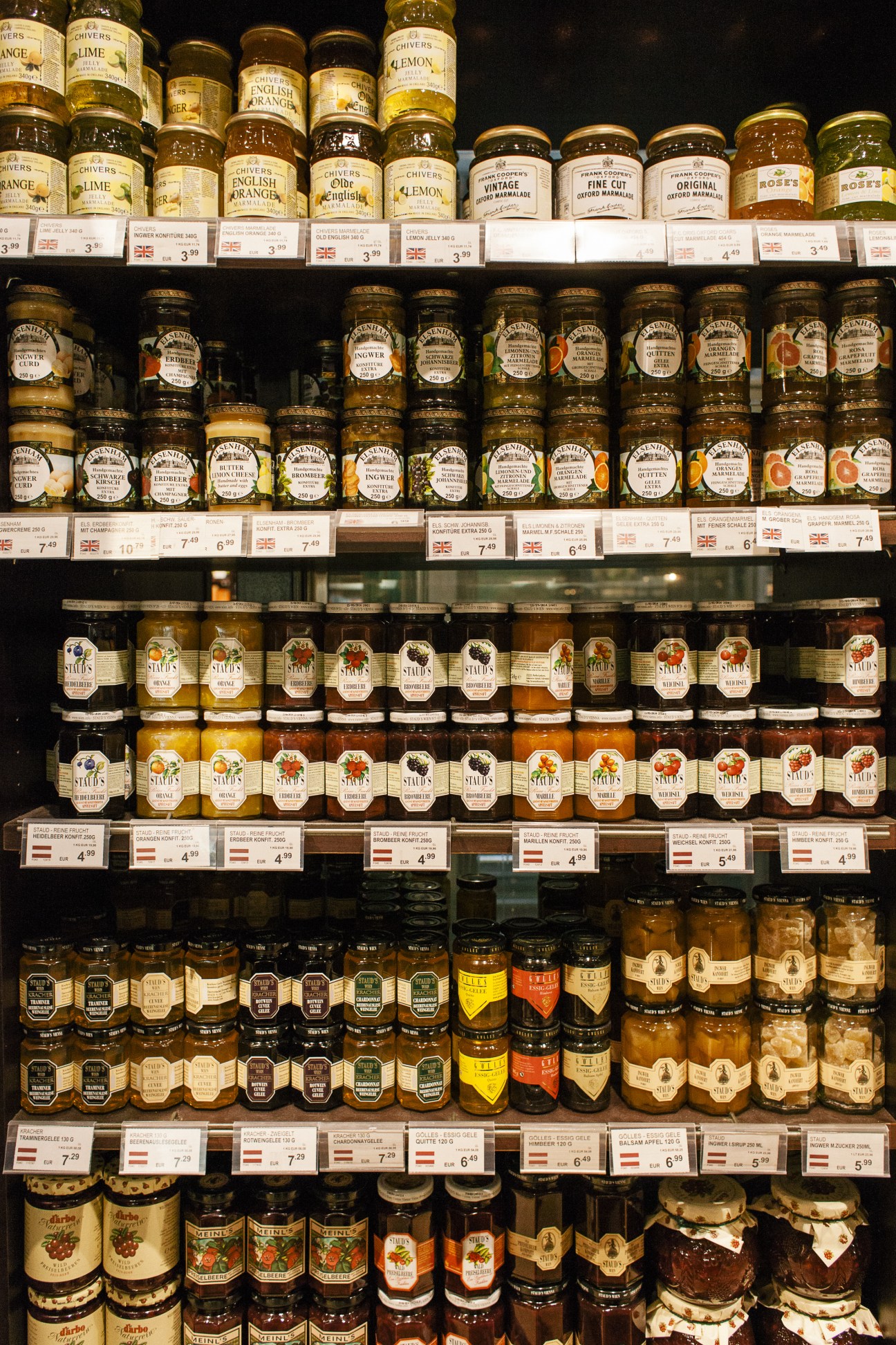 Shelves of glass jars with various preserves, spreads, and condiments, featuring brands like Chivers and Stute with price tags displayed.