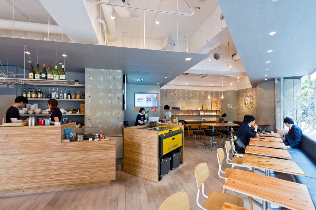 Interior of FabCafe Tokyo showing wooden counter, seating areas, and bright workshop-style design.