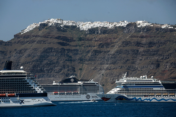 Large cruise ships sailing in blue waters past Santorini's white-washed cliffside buildings.