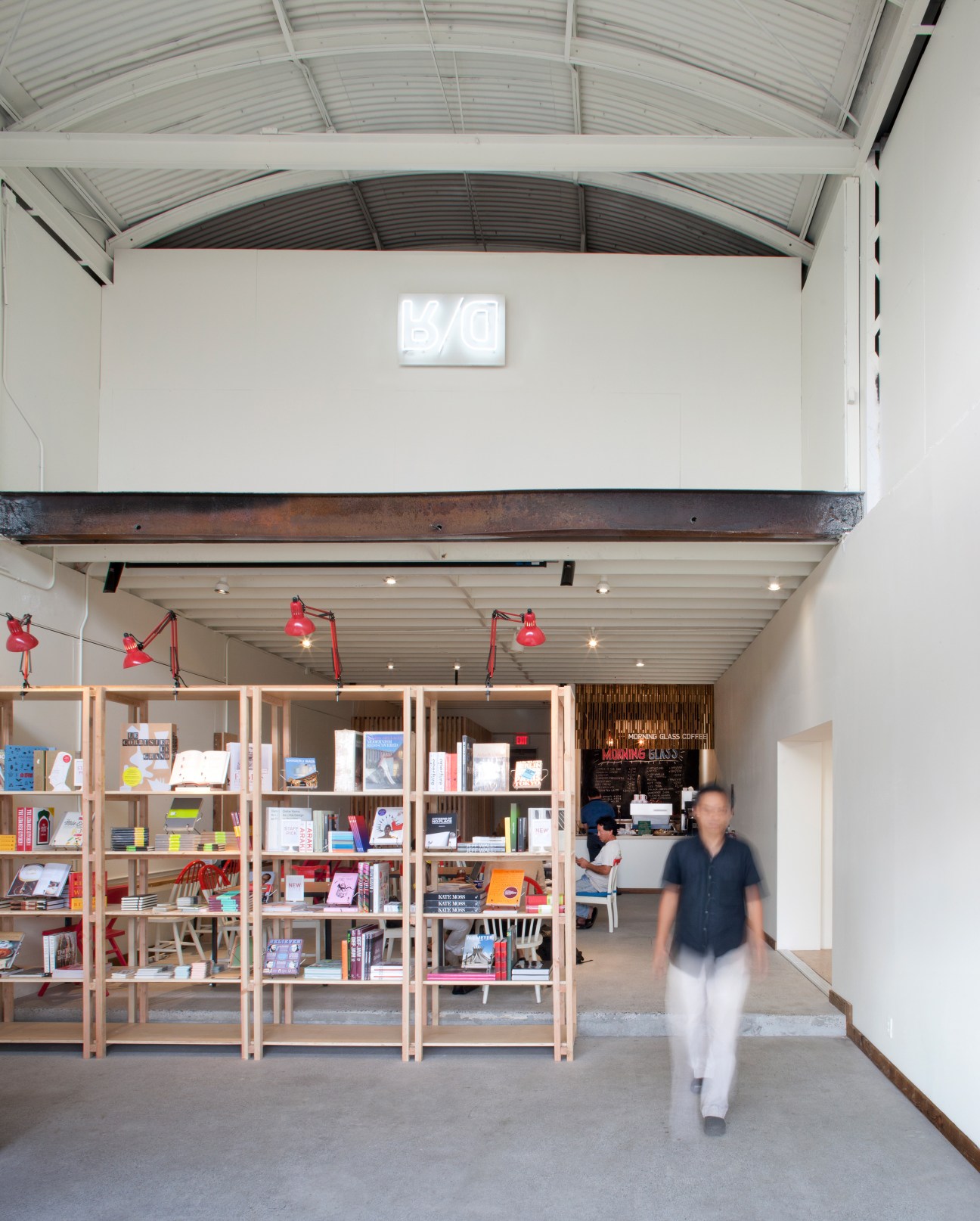 Modern bookstore interior with wooden shelving units displaying books and a person walking through the space