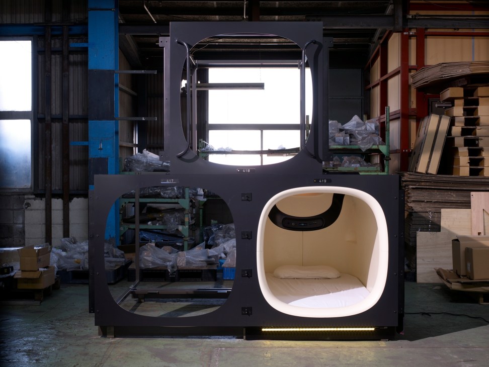 9 Hours capsule hotel sleeping pod prototype with illuminated interior in industrial workshop setting.
