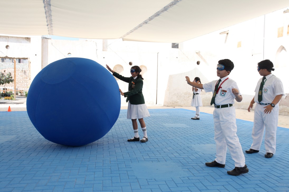 A large blue sphere in an outdoor space with people in uniforms interacting with it.