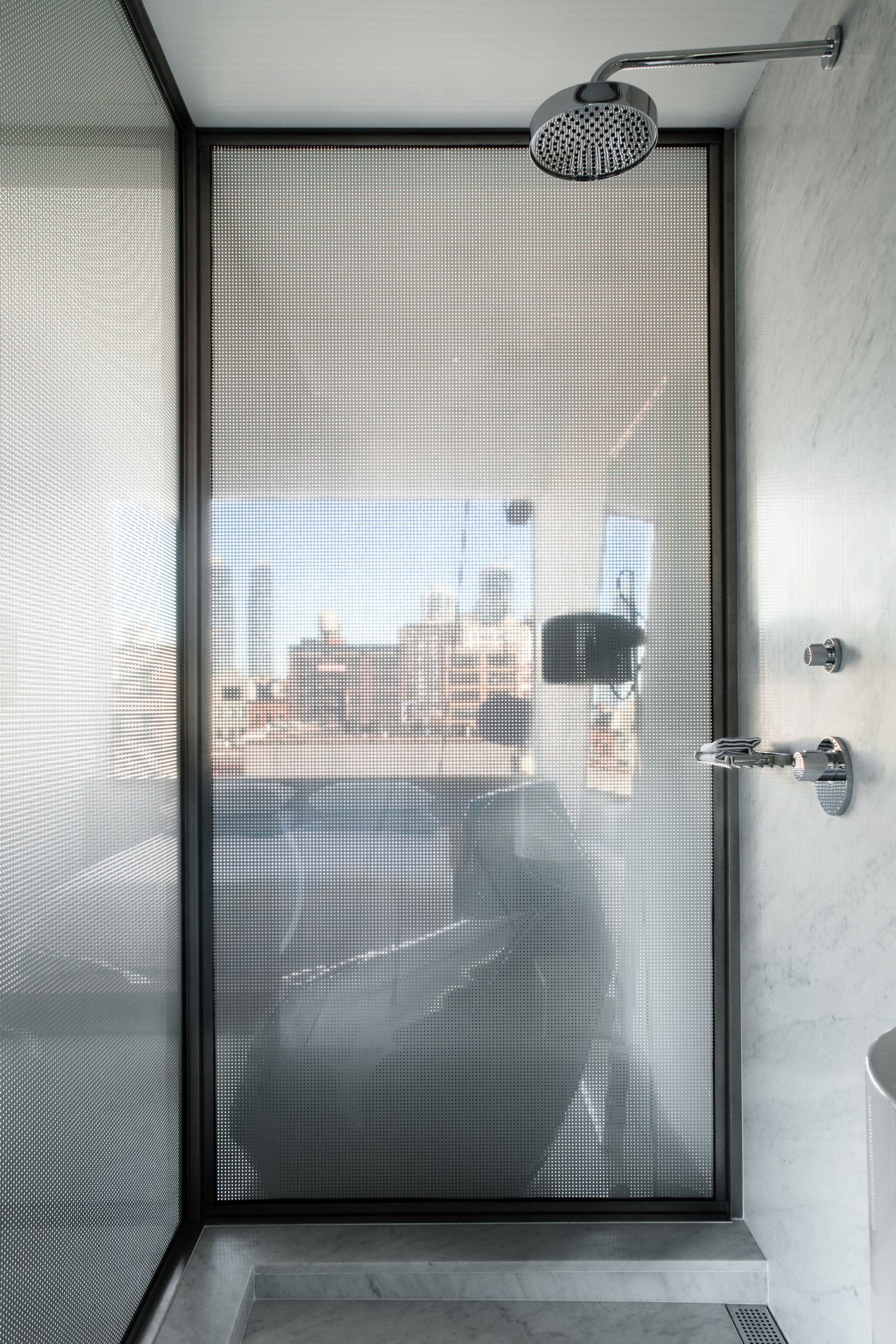 Modern hotel shower with rainfall showerhead and frosted glass enclosure overlooking Manhattan skyline.