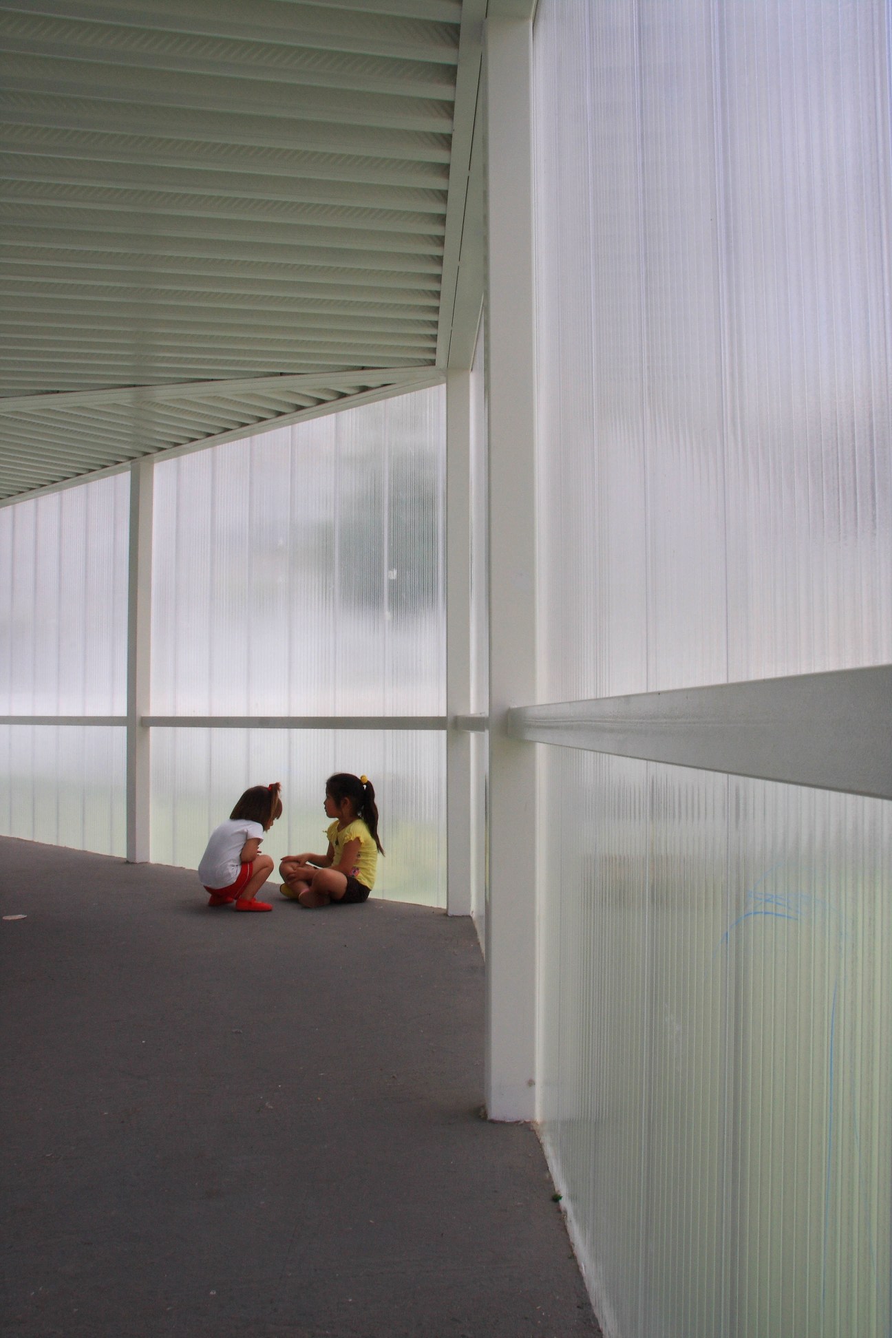 Two children sit on a polycarbonate gallery connecting the school's two separate entrances.