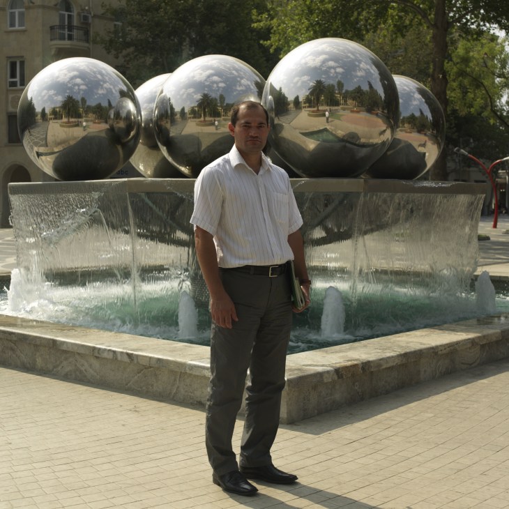 Man in white shirt standing in front of large reflective metal spheres in a public square.