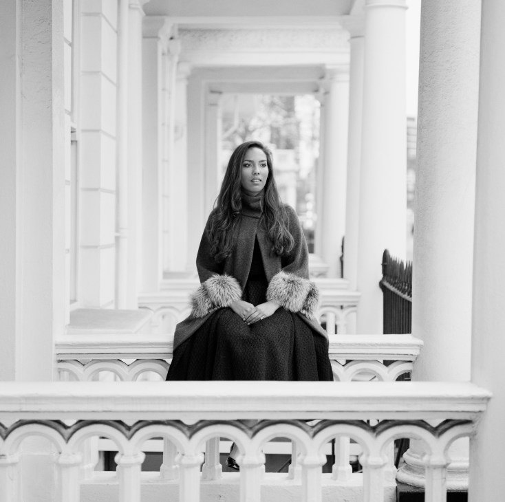 Princess Alia Idris al-Senussi sits on a white balcony wearing a dark coat with fur cuffs in a black and white portrait photograph.