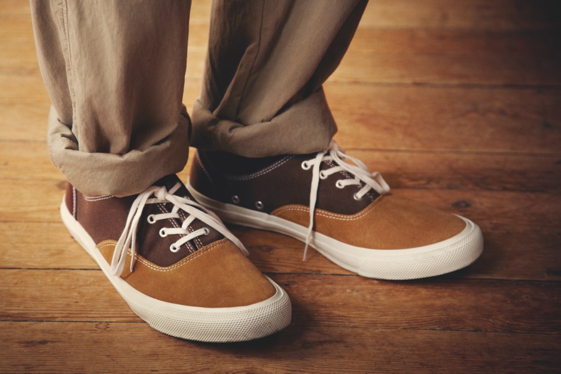 Person wearing tan trousers and brown-and-tan suede sneakers with white soles on a wooden floor.