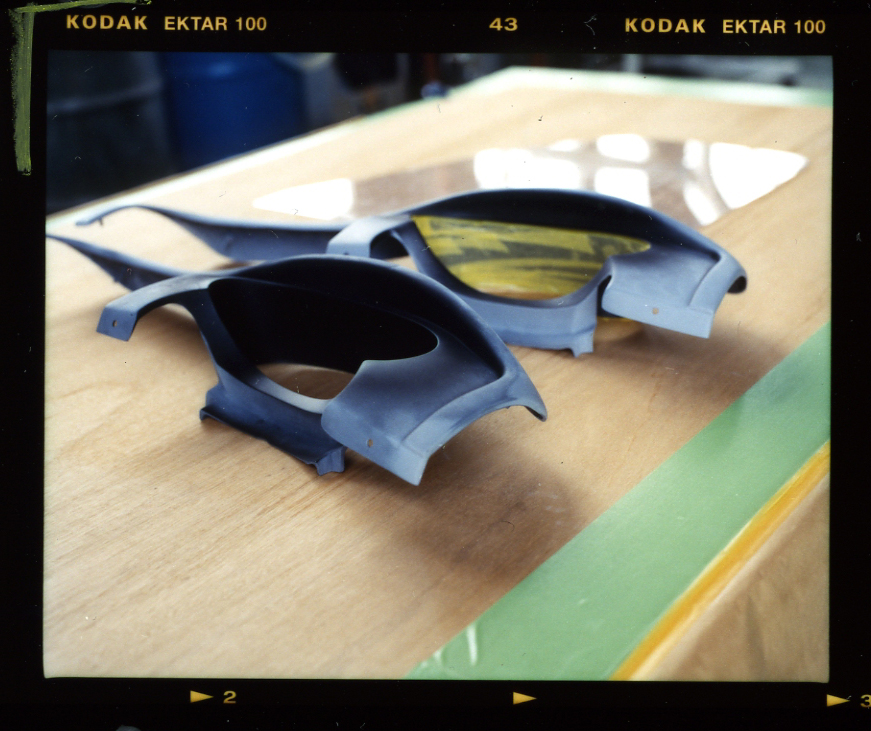Blue car body panels and parts displayed on a wooden work surface at Mitsuoka's factory.