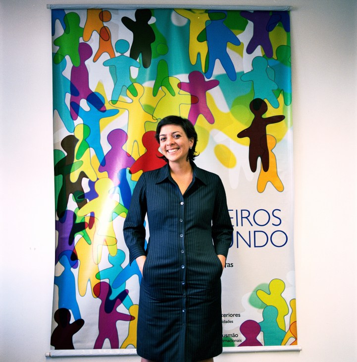 Adriana Telles Ribeiro stands before a colorful banner with silhouetted figures in various colors.