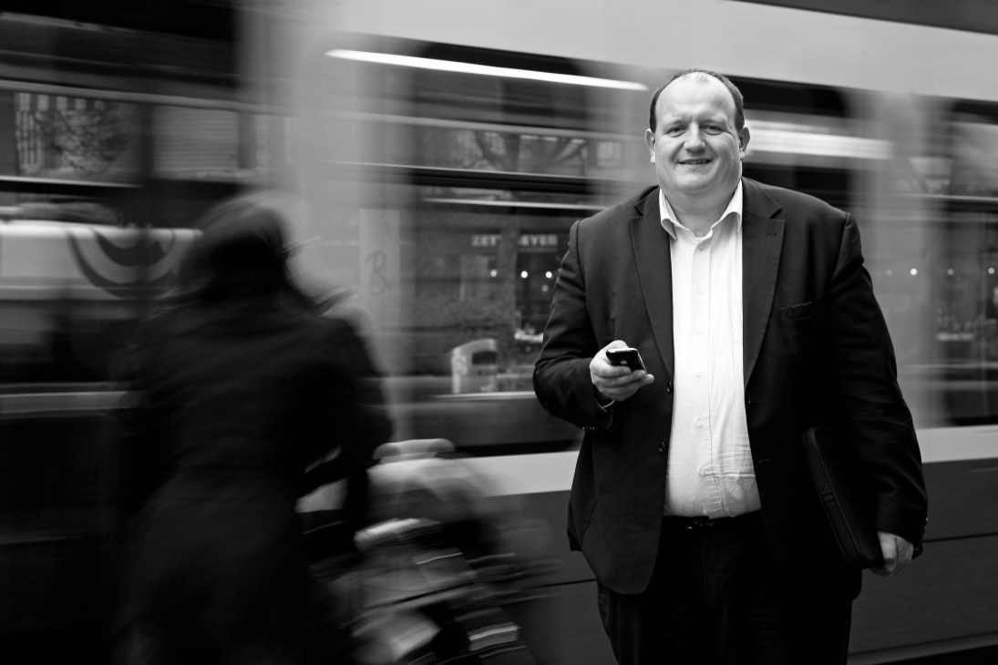 Dr Peter Hogenkamp, head of digital media at NZZ, walks past a blurred storefront holding a mobile device.