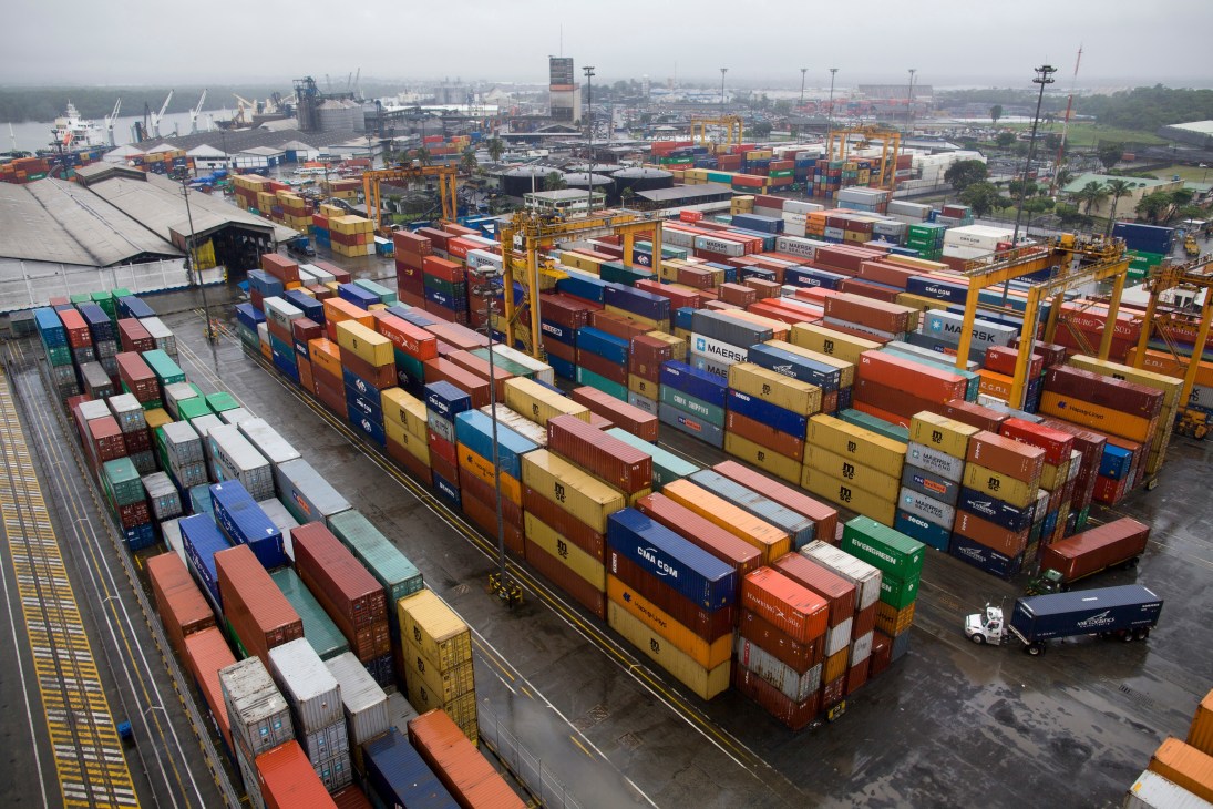 Aerial view of Buenaventura port with colorful stacked shipping containers, cargo ships, yellow cranes, and industrial facilities.